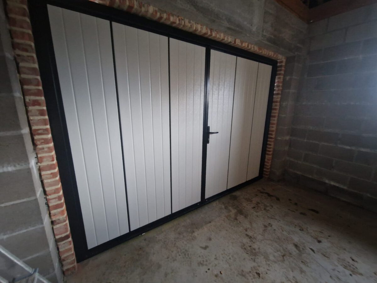 In de tuin gelegen, is een openslaande garagedeur met een full-line houtnerf structuur in RAL 9005 geïnstalleerd.