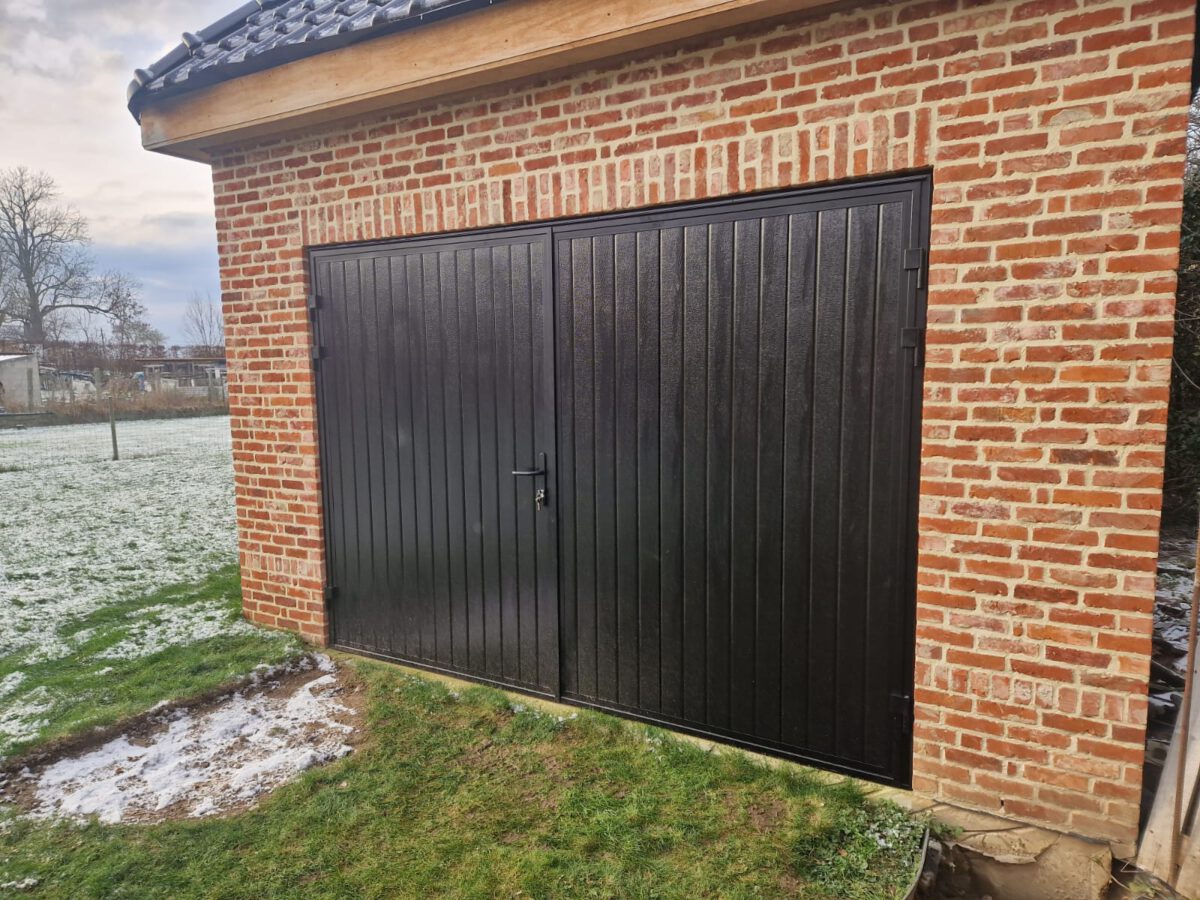Een garagedeur met full-line houtnerfstructuur in RAL 9005, die openslaat, is geplaatst in een garage achterin de tuin.