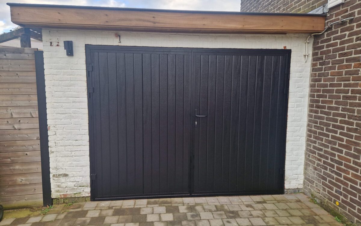 De openslaande garagedeur is uitgevoerd in een zwarte Full-Line houtnerf structuur met een verticale verdeling volgens RAL 9005.